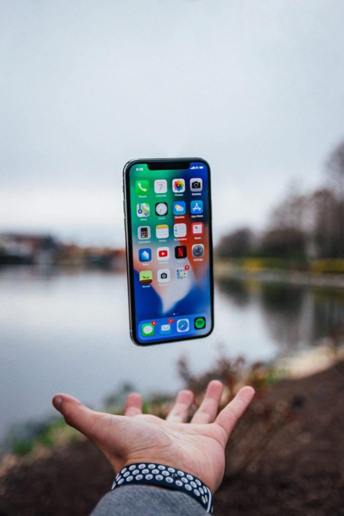 A smartphone displaying various mobile apps floating above a hand in an outdoor park setting with a lake in the background to showcase top eco-friendly apps