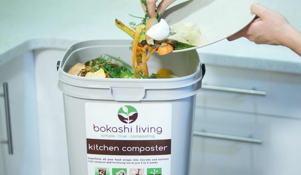 Food scraps being layered in a Bokashi composting bin with a sprinkling of bran on top.