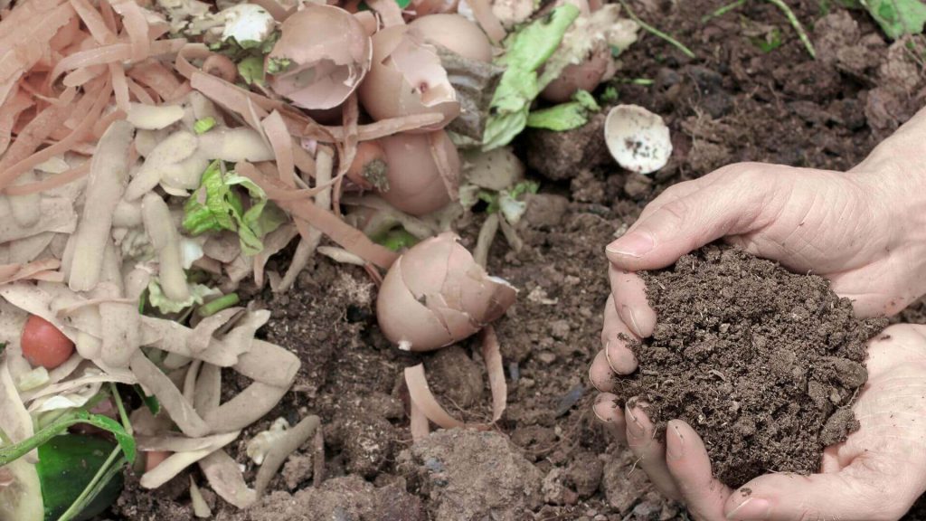 Person holding nutrient-rich dark finished compost soil in their hands over a garden bed.