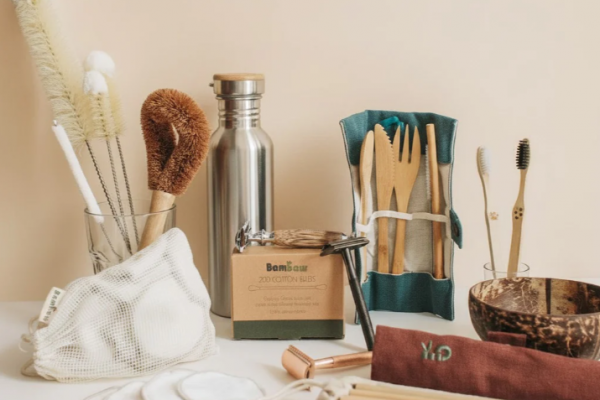 Collection of sustainable living tools including bamboo toothbrushes, reusable stainless steel water bottles, and cleaning brushes on a natural countertop.