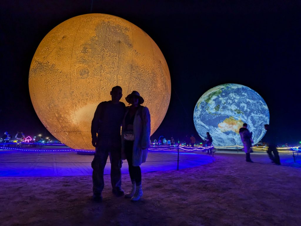 Image of two people standing in front of burning man earth art installation representing sustainability and protecting the earth. 
