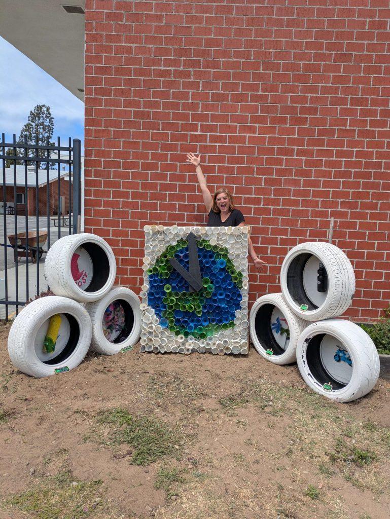 Is burning Man sustainable? This image of an Earth art installation made out of plastic water bottles and surrounded on each side with 3 white tires per side. The tires have images on the inside that represent ways we can help Earth.