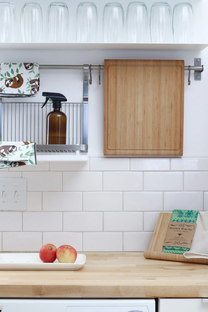 Minimalist zero-waste kitchen setup with wooden cutting board and eco-friendly cleaning spray in a small space.