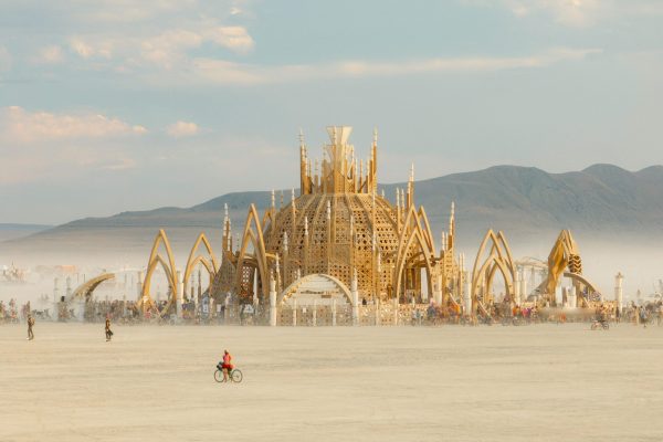 Is Burning Man sustainable? showcased with an image of a temple built in the middle of the desert and afterwards is taken down with the burning man "leave no trace" principles. Image of a wooden temple in the middle of Black Rock City.