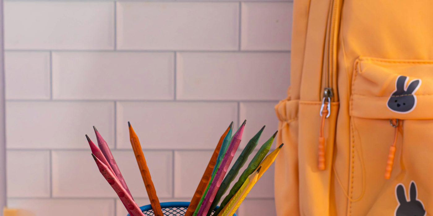 Yellow eco-friendly school backpack with colorful pencils in a blue cup on a desk.