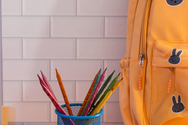 Yellow eco-friendly school backpack with colorful pencils in a blue cup on a desk.