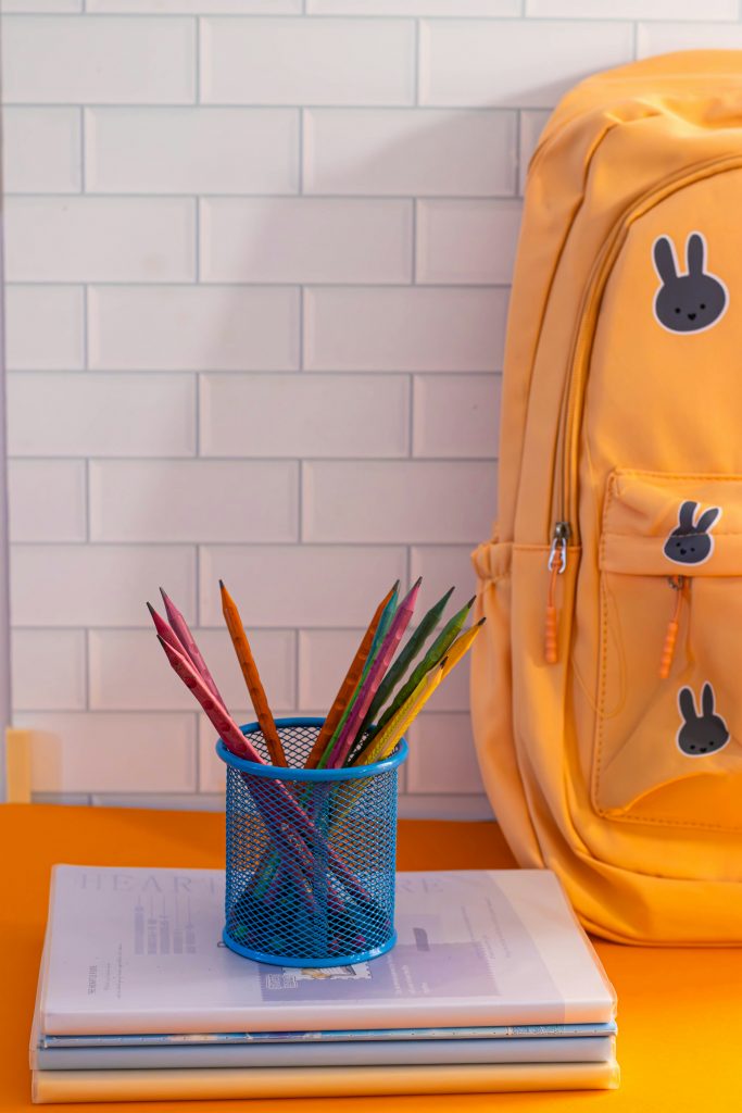 Yellow eco-friendly school backpack with colorful pencils in a blue cup on a desk.