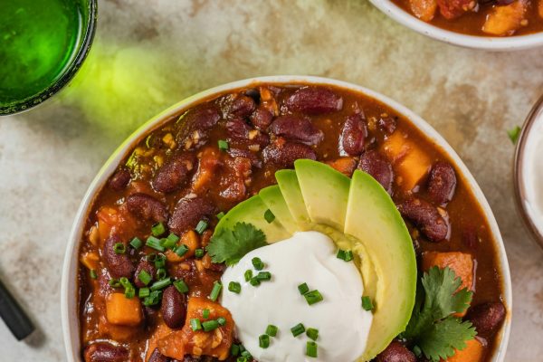 Image of best vegan chili plant-based with beans, veggies, avocado, and vegan sour cream on a table.