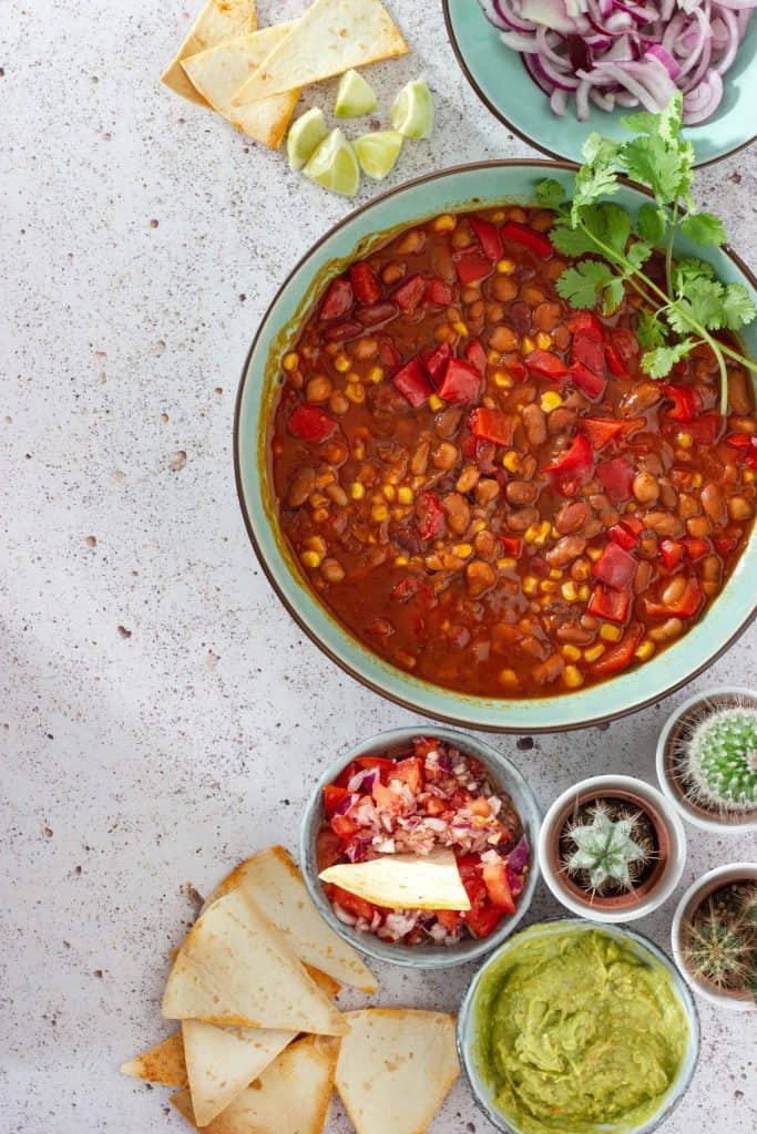 Image of best vegan chili overhead view of green bowl with fresh veggies and plant-based chili